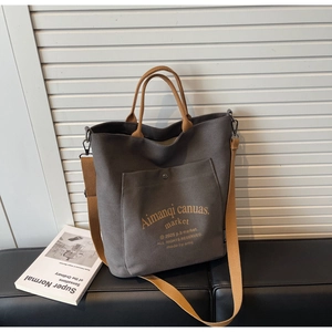 Detail view of dark grey canvas tote bag with yellow straps and vintage metal button pocket