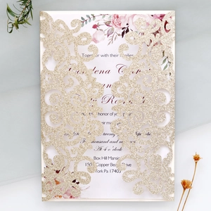 Intricate laser-cut gold glitter wedding invitation with elegant vine patterns and floral insert