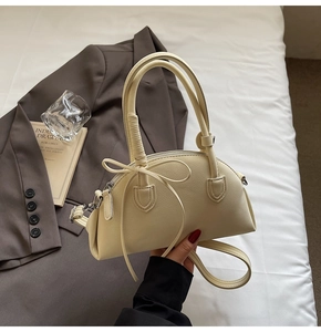 Close-up of beige lychee grain leather bag with decorative bow and handle detail