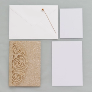 Detail of laser-cut gold glitter rose pattern invitation with envelope and blank insert cards