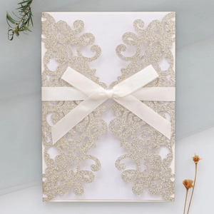 Detail of laser-cut wedding invitation with champagne gold glitter and silk ribbon bow