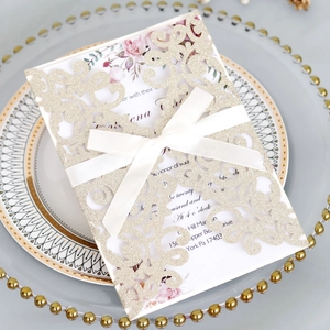 Close-up of laser-cut glitter wedding invitation with champagne floral patterns and white ribbon