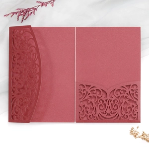 Detail of laser-cut burgundy invitation with intricate European floral vine patterns
