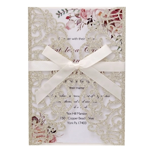 Detail of laser-cut champagne glitter wedding invitation with satin bow and floral insert