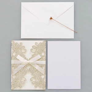 Detailed laser-cut gold glitter wedding invitation set with a white ribbon and envelope