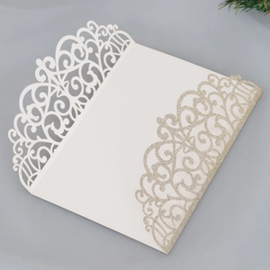 Detail of white laser-cut invitation with baroque patterns and gold glitter accents