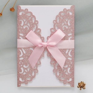 Close-up of pink glitter laser cut wedding invitation with elegant satin ribbon bow