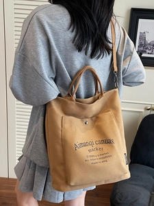 Khaki canvas tote bag with front pocket and adjustable strap worn by a model