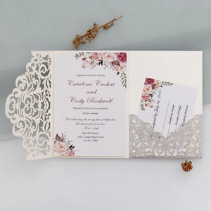Flat lay of laser-cut wedding invitation set with floral card and silver glitter pocket
