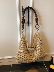 Large woven straw tote bag with beaded straps hanging on white closet door for vacation