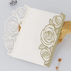 Detail of laser-cut glitter rose design on a gold and white wedding invitation card