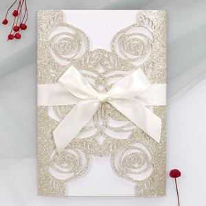 Detail view of laser-cut rose gold glitter invitation featuring a white satin ribbon bow