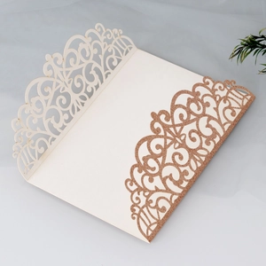 Macro detail of laser-cut cream wedding invitation with rose gold glitter finish