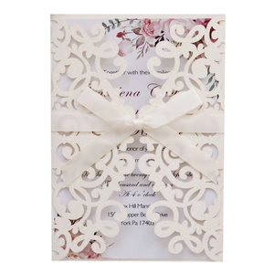 Detail of laser-cut glitter wedding invitation with elegant satin bow and floral insert
