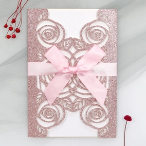 Detail of pink glitter wedding invitation with laser-cut rose design and satin ribbon bow