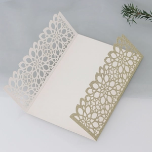 Close-up of laser-cut cream wedding invitation with gold glitter and floral patterns