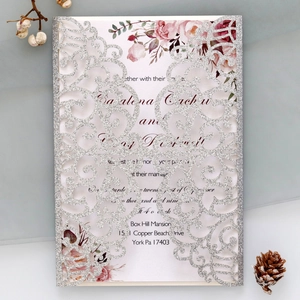 Detail of laser-cut glitter invitation with floral insert on a natural background
