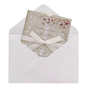 Close-up of golden laser-cut wedding invitation set with glitter cover and ribbon