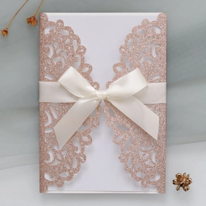 Detail of rose gold glitter laser-cut invitation with elegant white satin bow ribbon