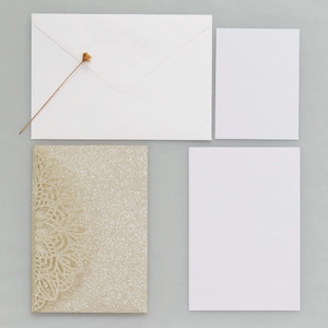 Detail of laser-cut gold glitter wedding invitation set with envelopes and dry flower