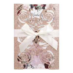 Detail of rose gold glitter wedding invitation with laser-cut floral pattern and satin bow