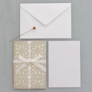 Detail of laser-cut glitter wedding invitation with white ribbon bow and envelopes