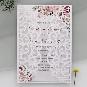 Detailed laser-cut wedding invitation with elegant white floral patterns and scrollwork