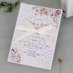 Detailed laser-cut white wedding invitation with cream silk ribbon and floral inner card