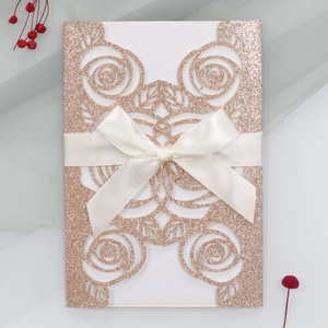 Macro view of rose gold glitter wedding invitation with laser-cut floral patterns and ribbon