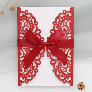 Close-up of laser-cut red glitter wedding invitation with elegant satin bow detail