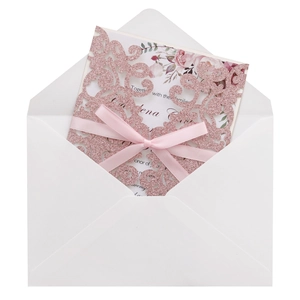 Close-up of pink glitter laser-cut wedding invitation with silk bow and white envelope