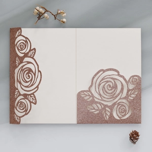 Macro detail of laser-cut rose floral wedding invitation with rose gold glitter texture