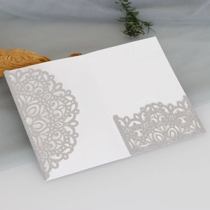 Detail of laser-cut silver glitter wedding invitation with elegant lace pattern and pocket