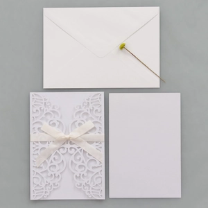 Flat lay of laser-cut white wedding invitation set with silk bow and V-flap envelope