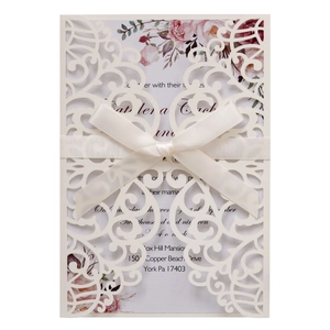 Detail of laser-cut wedding invitation with cream floral sleeve and satin ribbon bow