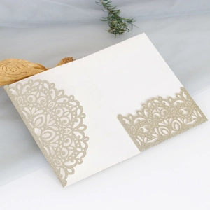 Macro shot of white laser-cut wedding card with intricate gold glitter floral pattern