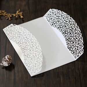 Detail of laser-cut white wedding invitation with elegant vine patterns on wood background