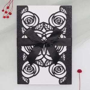 Detail of laser-cut rose patterns on black glitter wedding invitations with a ribbon