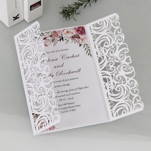 Detail of white laser-cut wedding invitation featuring intricate floral scroll patterns