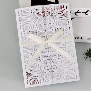 Detail of white laser cut wedding invitation with floral pattern and cream satin ribbon