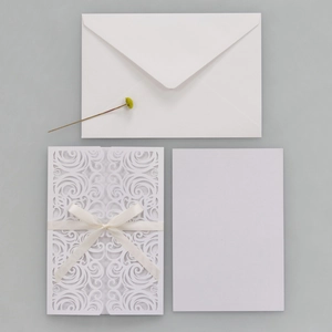 Macro shot of white laser-cut floral wedding invitation with cream ribbon bow detail
