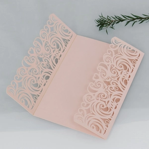 Macro detail of blush pink laser-cut wedding invitation with intricate heart scroll patterns