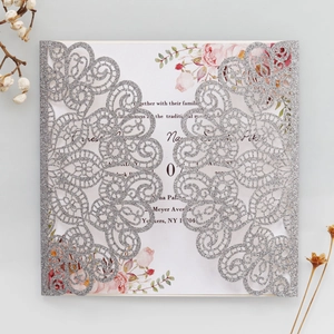 Detail of silver glitter laser cut wedding invitation with floral insert on grey background