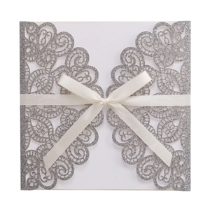 Detail showing laser-cut silver glitter wedding invitation with ivory ribbon bow