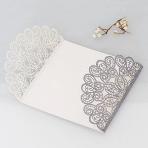 Detailed laser-cut mandala lace pattern on ivory invitation card with silver glitter