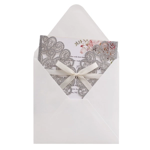 Detail of silver glitter laser-cut lace invitation with white satin bow and floral inner card