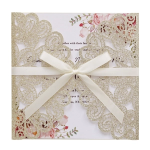 Close-up of glitter champagne gold laser-cut wedding invitation with ivory ribbon and floral insert