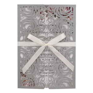 Elegant laser-cut silver wedding invitation with intricate scrollwork and cream satin bow