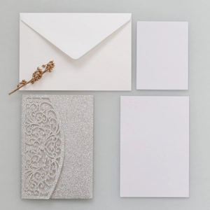 Vue à plat d'une invitation de mariage argentée pailletée découpée au laser avec enveloppe