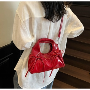 Détail du sac rouge en cuir verni avec nœuds et texture plissée sur les escaliers